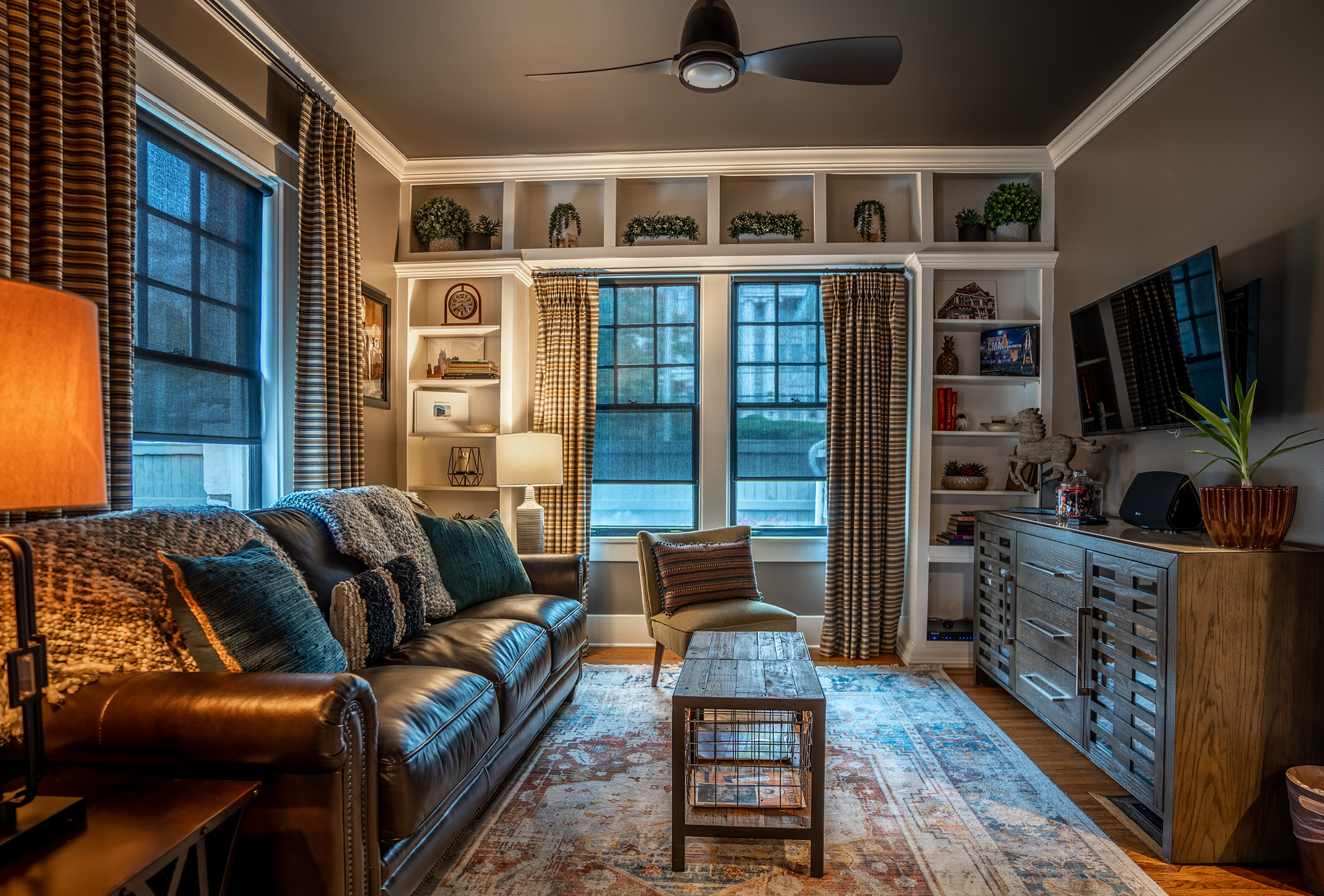 A large leather couch and TV in a cozy living room with lots of natural light